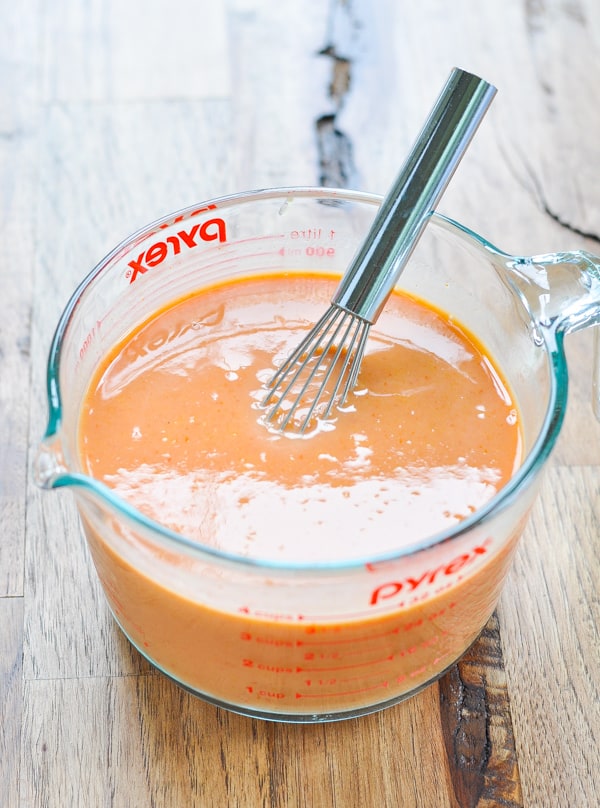 Enchilada sauce in a glass measuring cup with a whisk