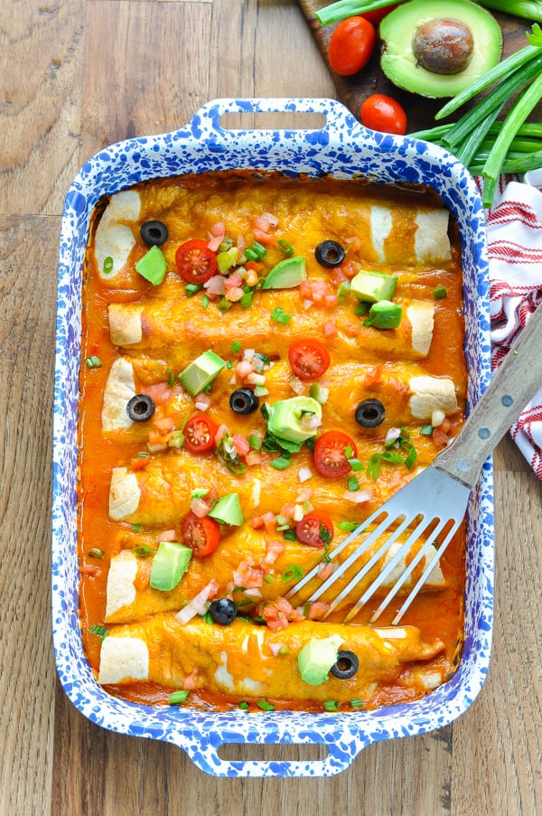 Long overhead image of easy beef enchiladas in a baking dish with a spatula