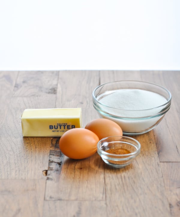 The additional ingredients needed to make Southern sweet potato casserole -- butter, two eggs, a bowl of sugar, and a smaller bowl of spices -- sitting on a wooden table.