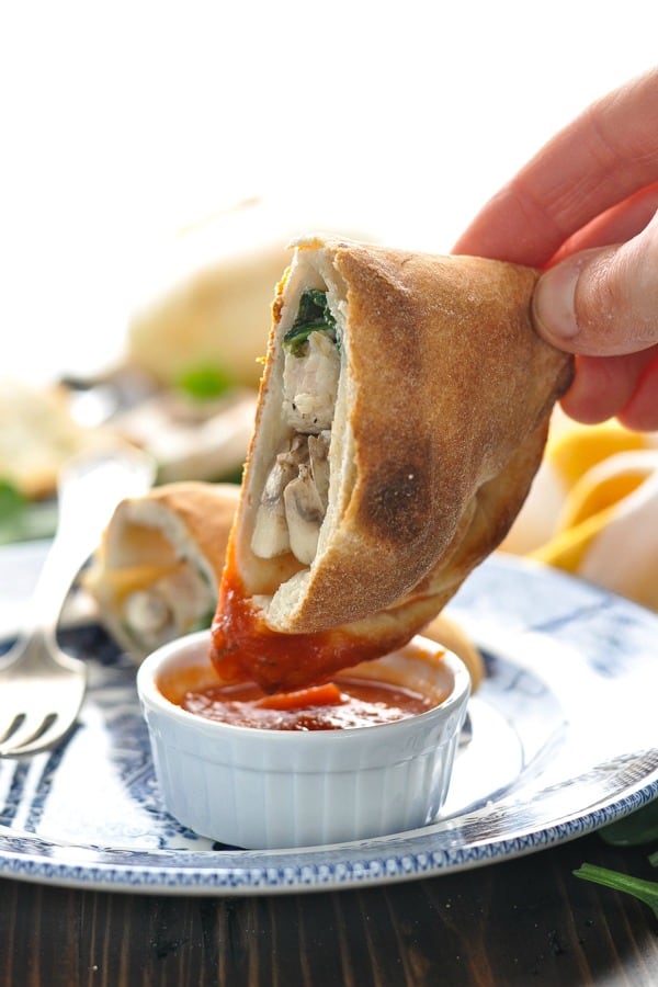 Dipping chicken and spinach calzone in tomato sauce