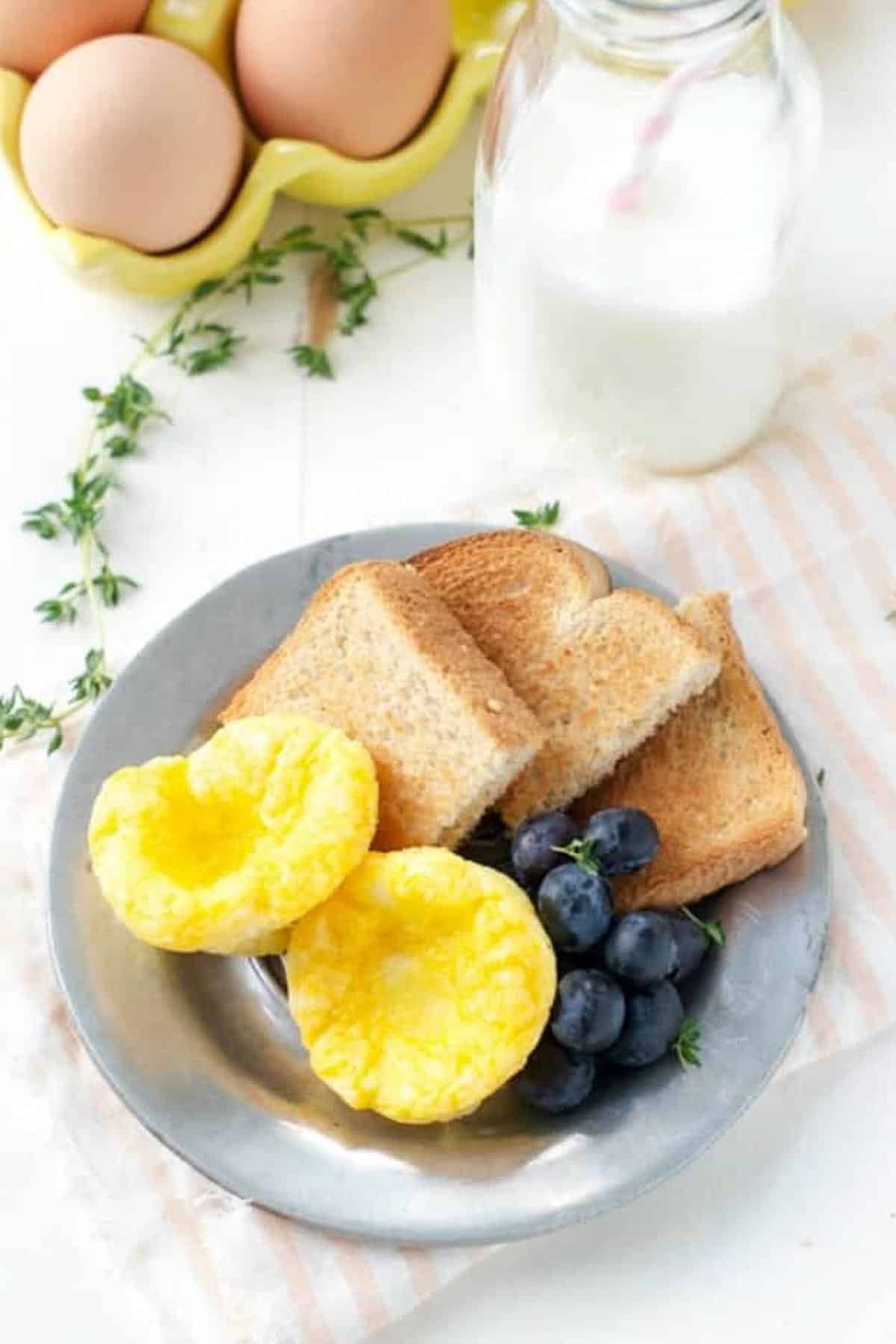 Overhead shot of a plate of mini egg bites with toast and fruit on a white table.