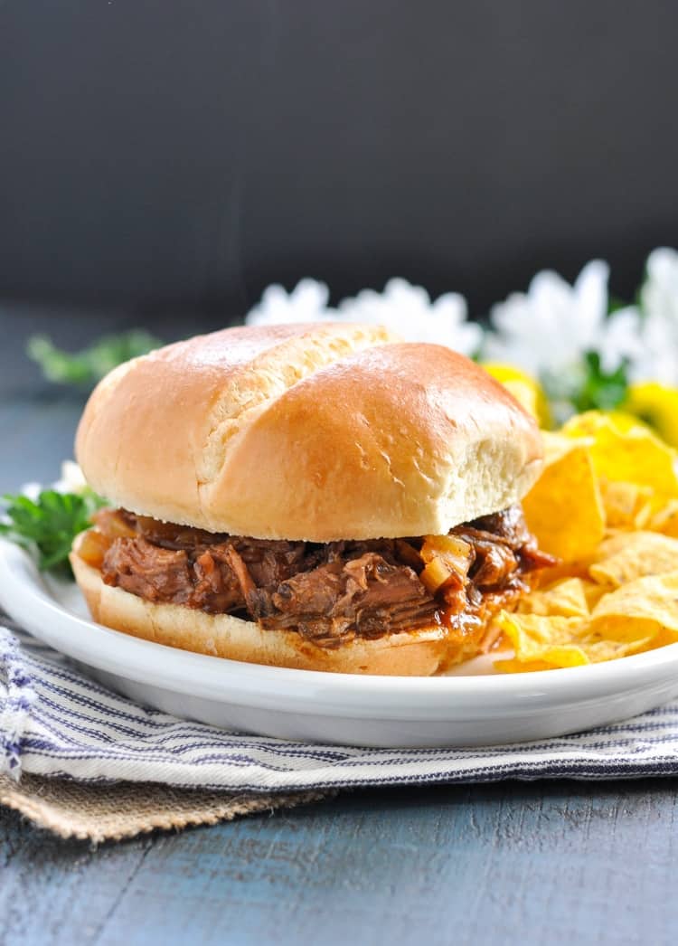 Slow cooker beef bbq on a bun sitting on a white plate