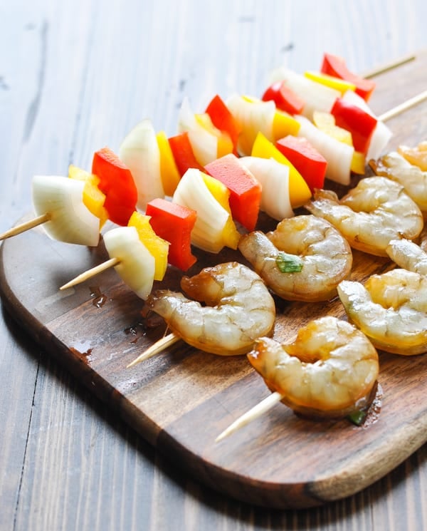 Raw shrimp skewers and vegetable skewers on a cutting board