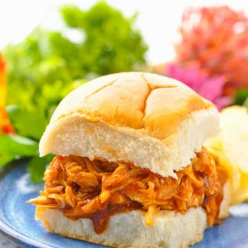 Pulled BBQ Chicken in Crock Pot served on a sandwich roll and placed on a blue plate