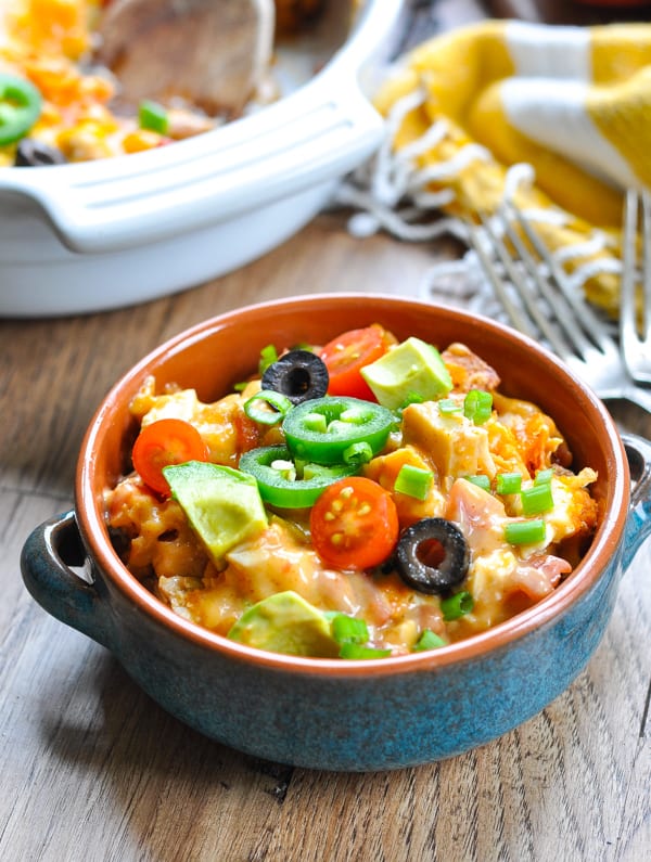 Bowl of chicken taco casserole in dish and topped with tomatoes olives avocados