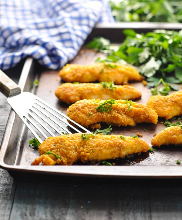 Crispy chicken tenders baked on sheet pan with spatula