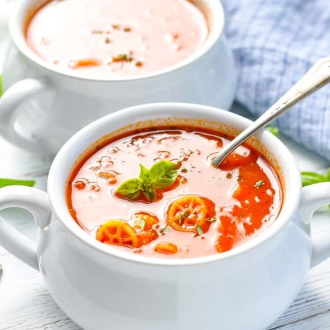 Two white bowls filled with tomato marinara soup topped with basil