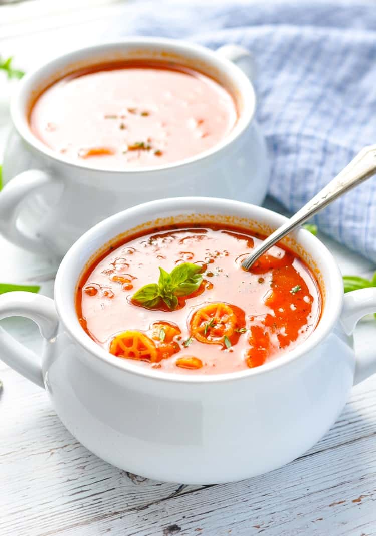 Two white bowls filled with tomato marinara soup topped with basil