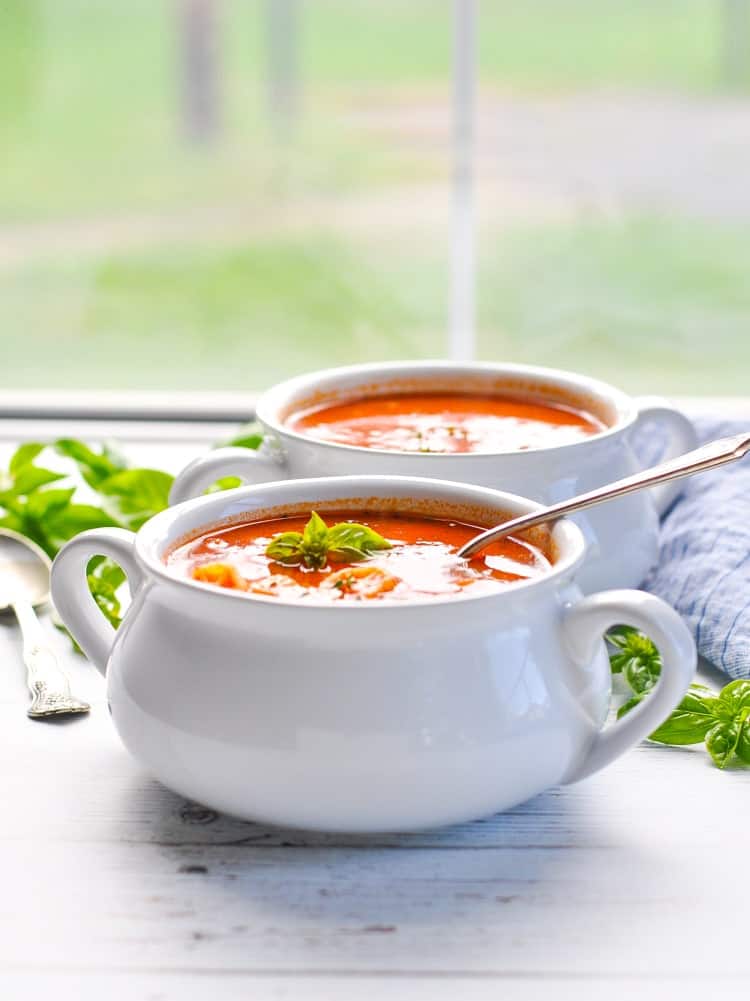 A side shot of white bowl of Marinara soup in front of a window