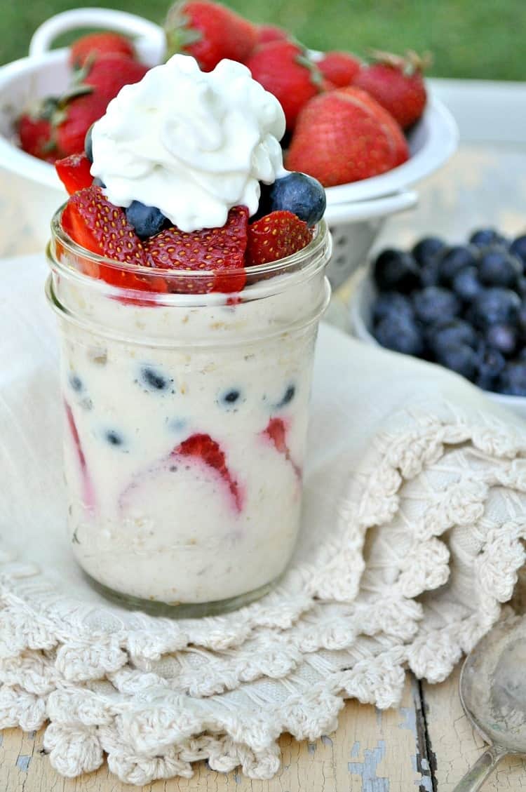 A small mason jar filled with strawberry overnight oats, topped with sliced strawberries, blueberries, and a dollop of whipped cream. 