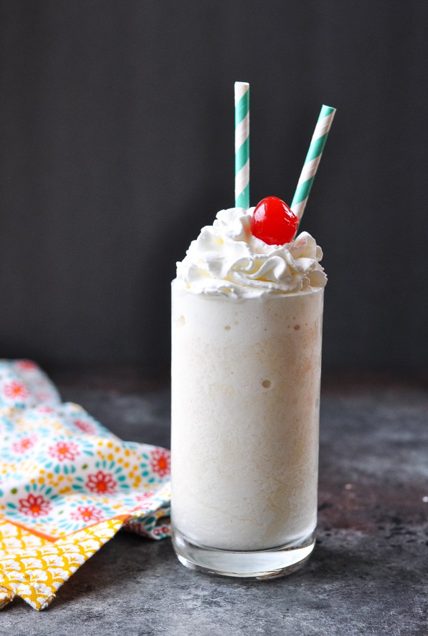 A large pineapple protein smoothie served in a glass, topped with whipped cream and a cherry.