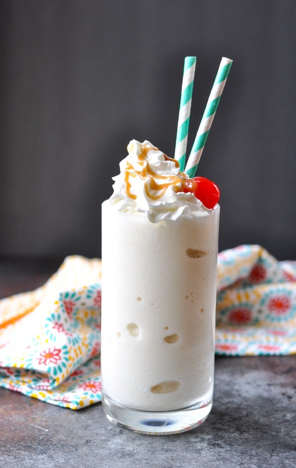 A pineapple protein shake served in a glass, topped with a cherry, whipped cream, and a drizzle of caramel syrup.