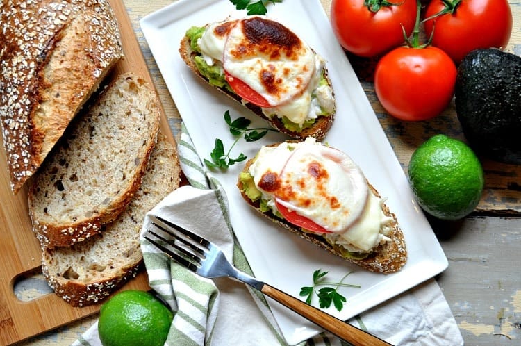 Two open faced crab melts with avocado and tomato on a white rectangle plate