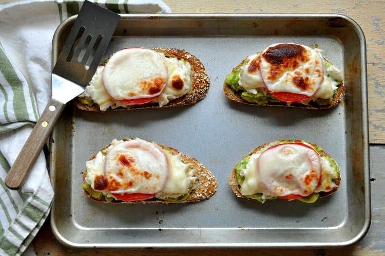 Four open faced crab melts on a baking tray with a spatula