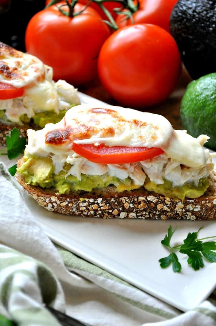 A close up of an avocado and crab melt topped with cheese and tomato