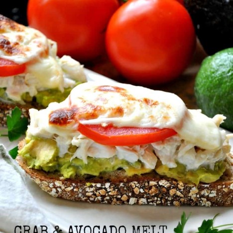 An open faced avocado and crab melt topped with a tomato on a plate