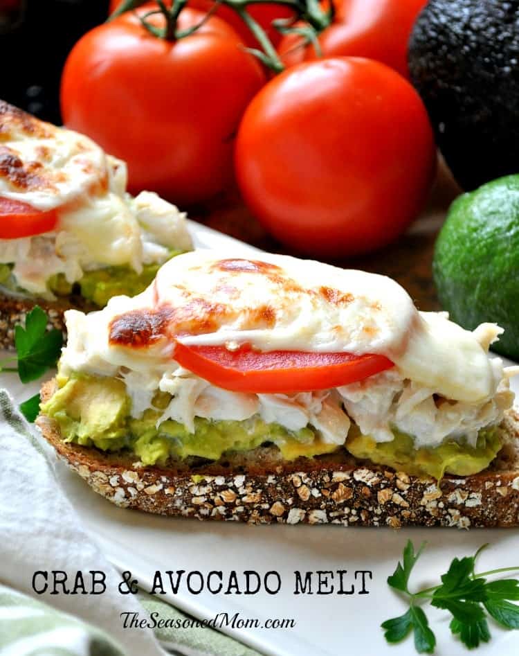 An open faced avocado and crab melt topped with a tomato on a plate