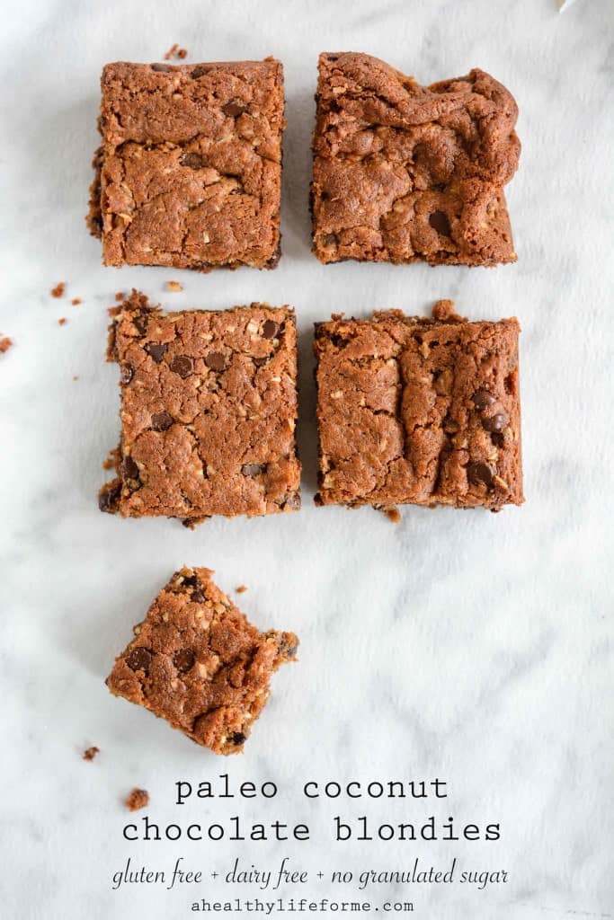 AN overhead image of five coconut chocolate chip brownies lined up on parchment paper.