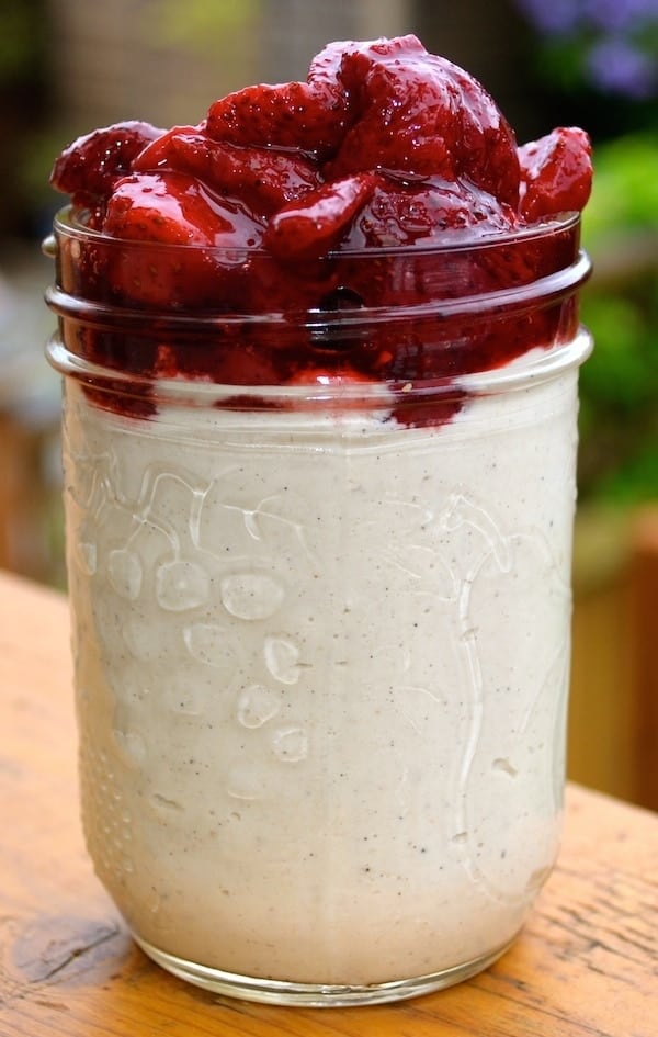A small mason jar filled with a vanilla bean cream and topped with roasted strawberries.