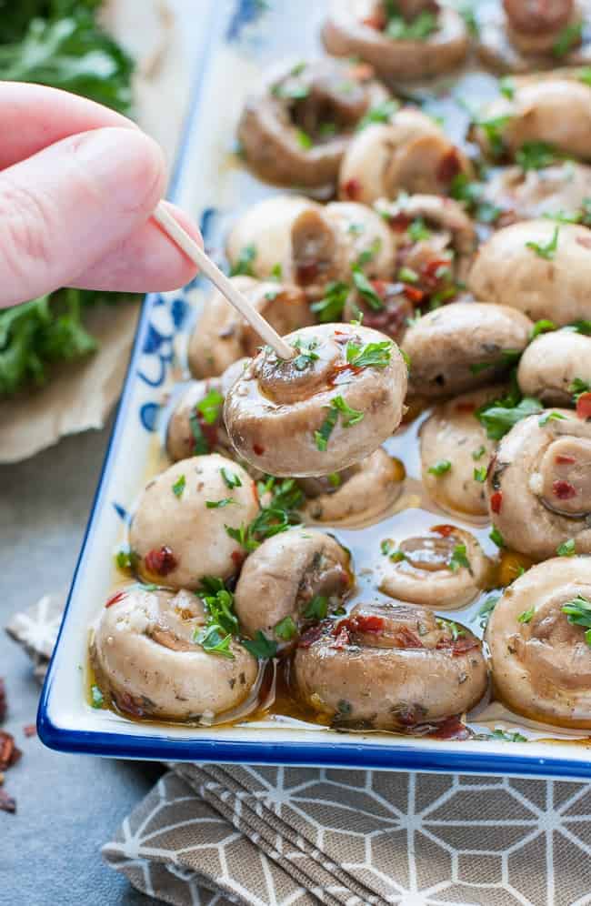 A dish full of marinated button mushrooms, with an oil-based sauce and herbs.