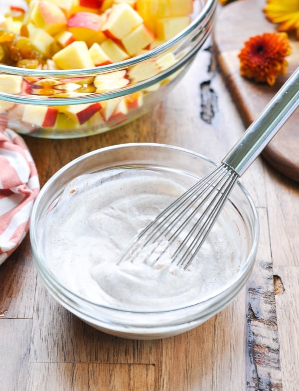 A small glass bowl filled with a creamy greek yogurt and mayonnaise dressing, mixed together with a wire whisk.