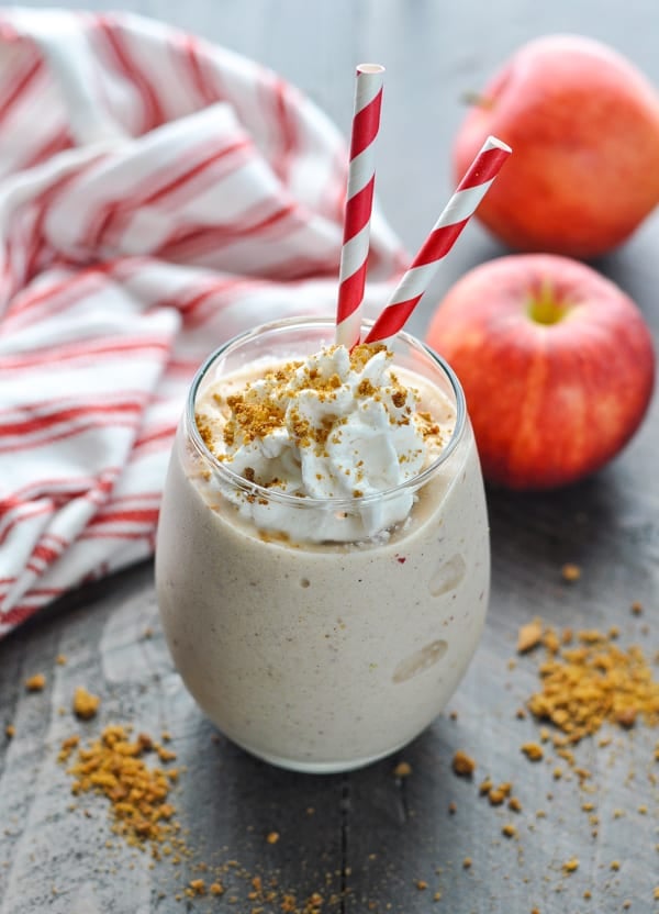 Apple pie protein smoothie in a glass garnished with whipped cream and crushed gingersnap cookies
