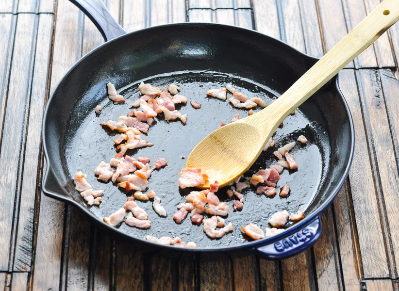 Crisp bacon in cast iron skillet with wooden spoon