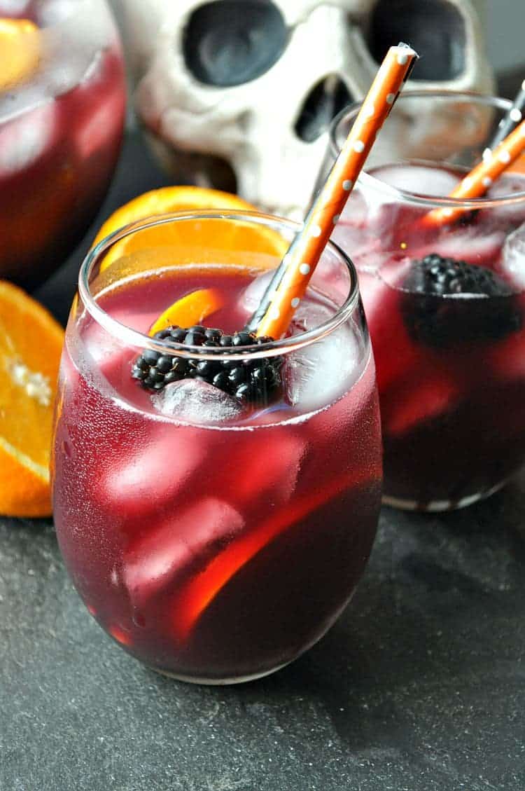 A close up image of two ice-cold glasses of red wine sangria, paired with fresh orange slices and blackberries for garnish.