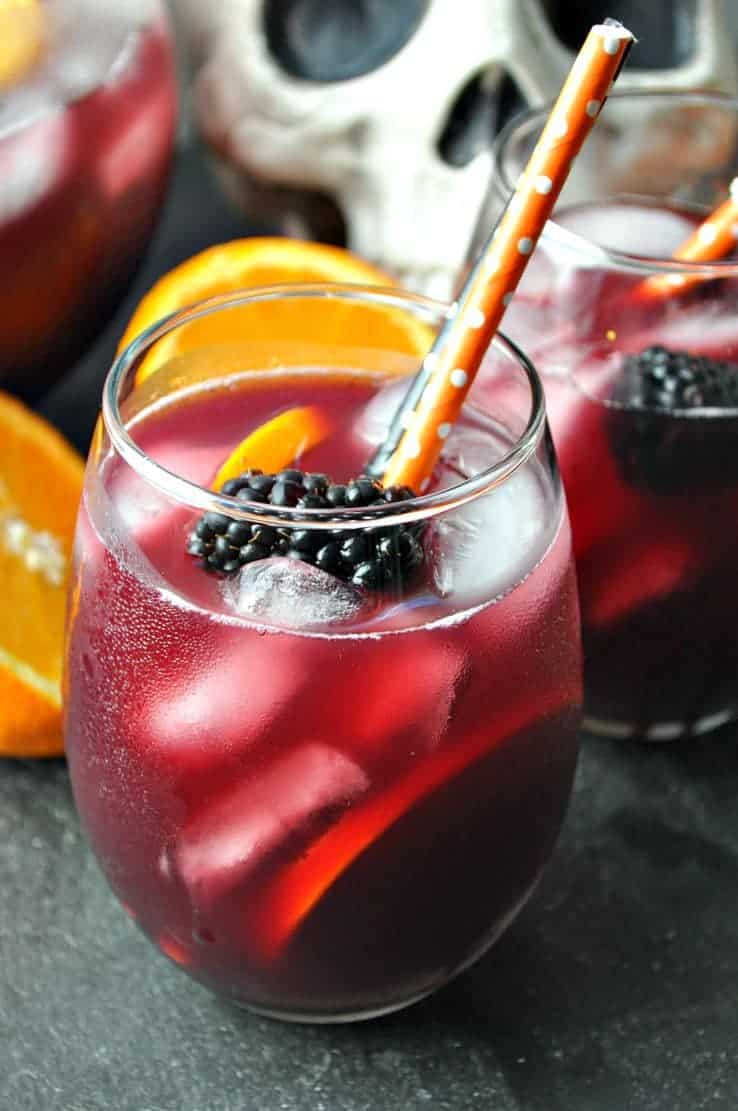 An ice-cold glass of red wine Sangria garnished with orange slices and blackberries.