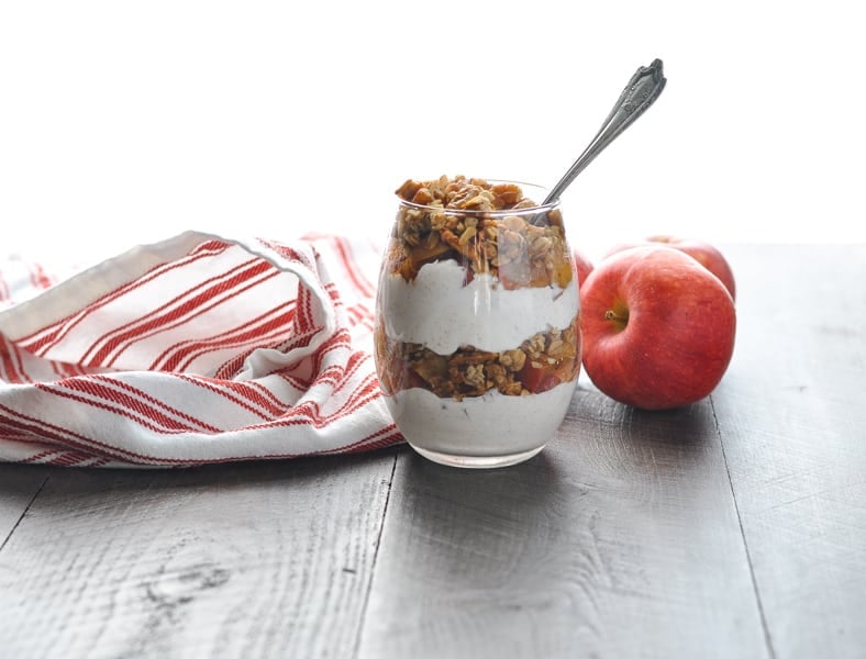 Apple Crisp Yogurt Parfait in a glass with a spoon and apples in background