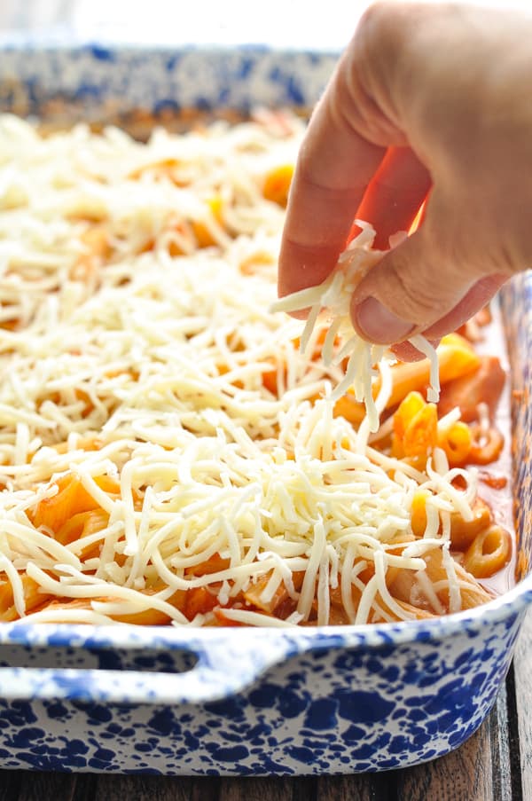 Sprinkling mozzarella over top of Chicken Parmesan Casserole
