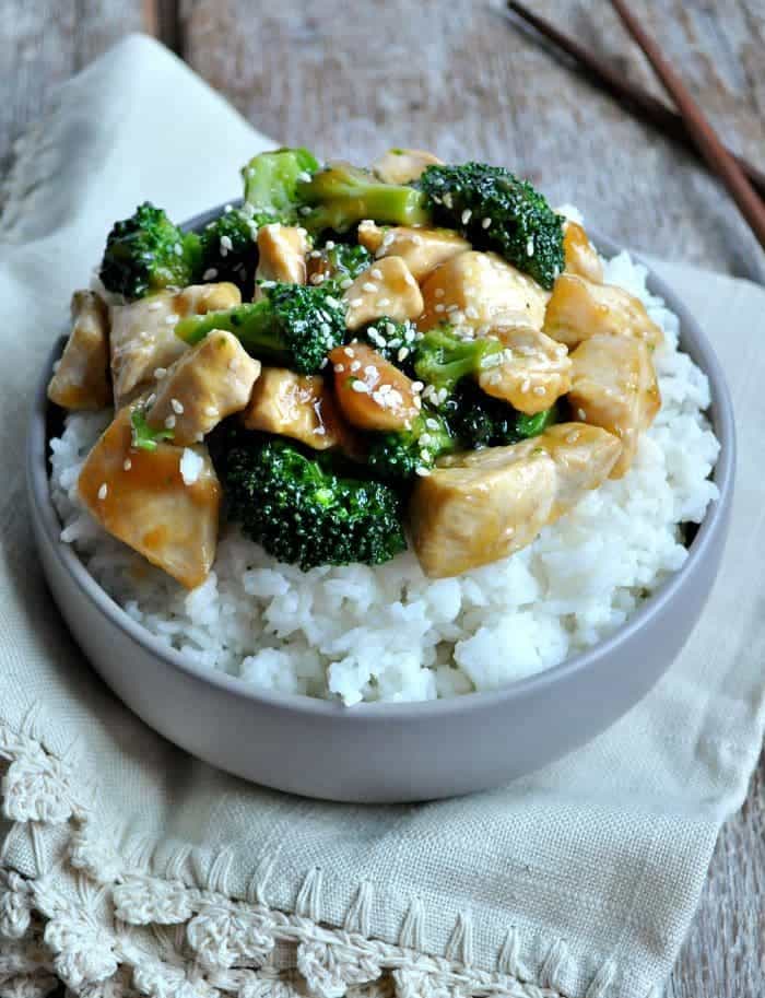 A close up of orange chicken and broccoli in a bowl with rice