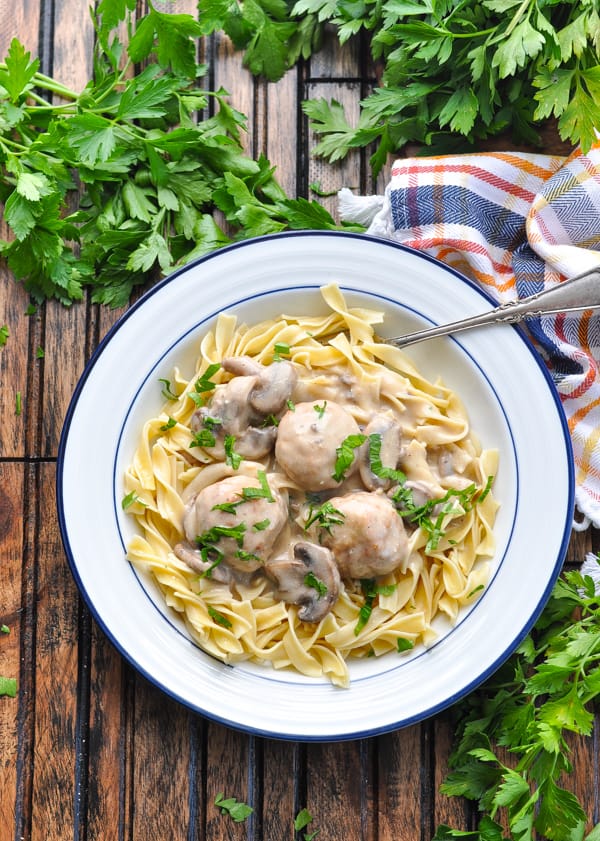 Overhead image of bowl of Slow Cooker Meatball Stroganoff with egg noodles and parsley.