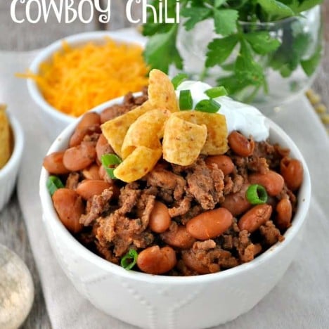A cowboy chili in a white bowl topped with green onions and sour cream