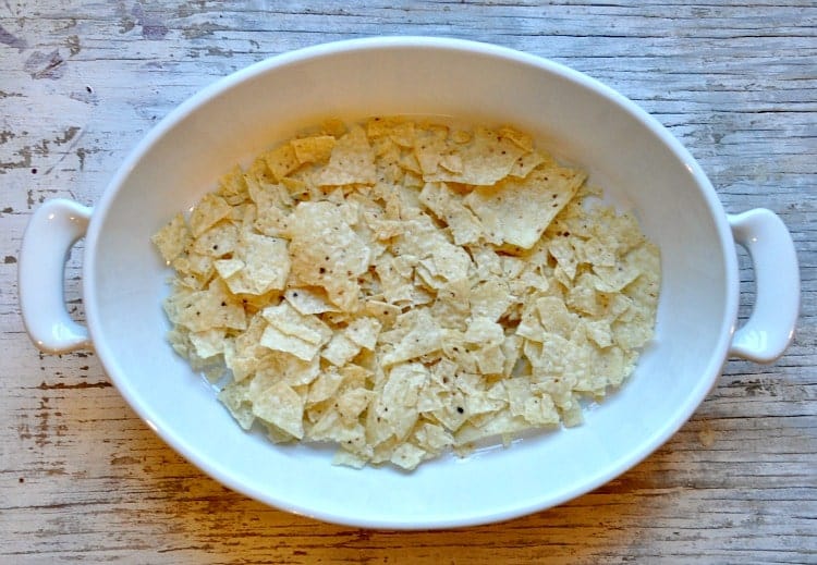 An overhead image of crushed tortilla chips spread on the bottom of a white casserole dish.
