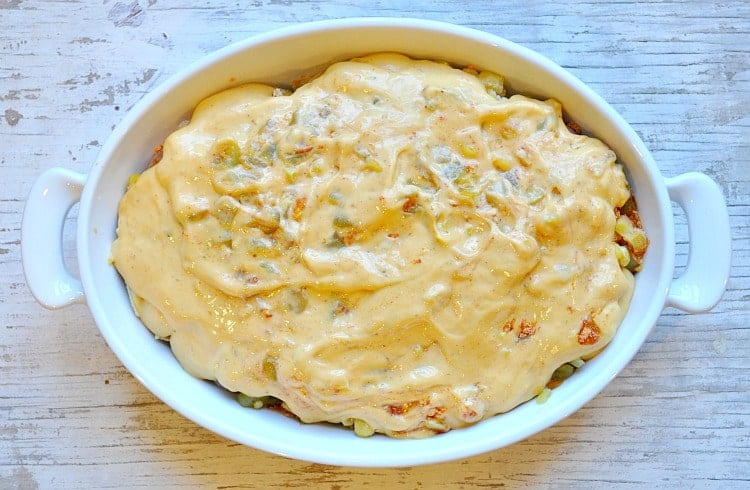 An overhead image of a casserole dish of chicken taco bake topped with a creamy cheese soup mixture before baking.