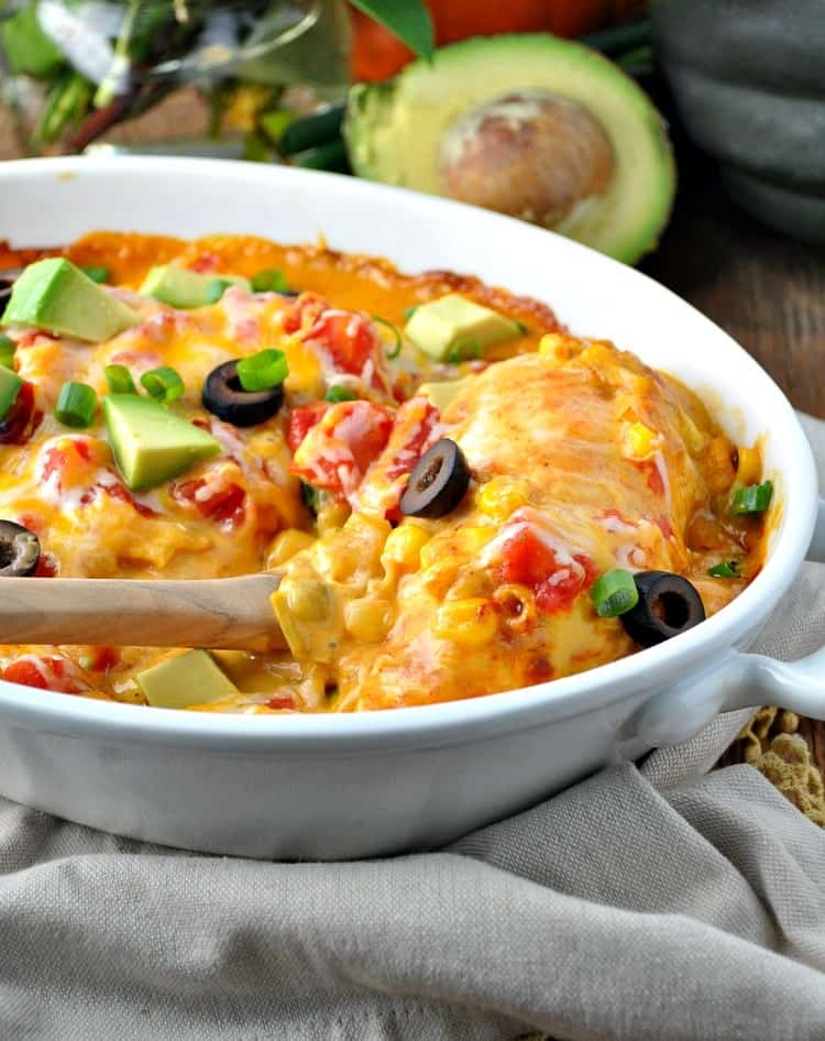 A close up image of cheesy dump and bake chicken taco casserole, topped with melted cheese, tomatoes, black olives, avocado, and green onions.