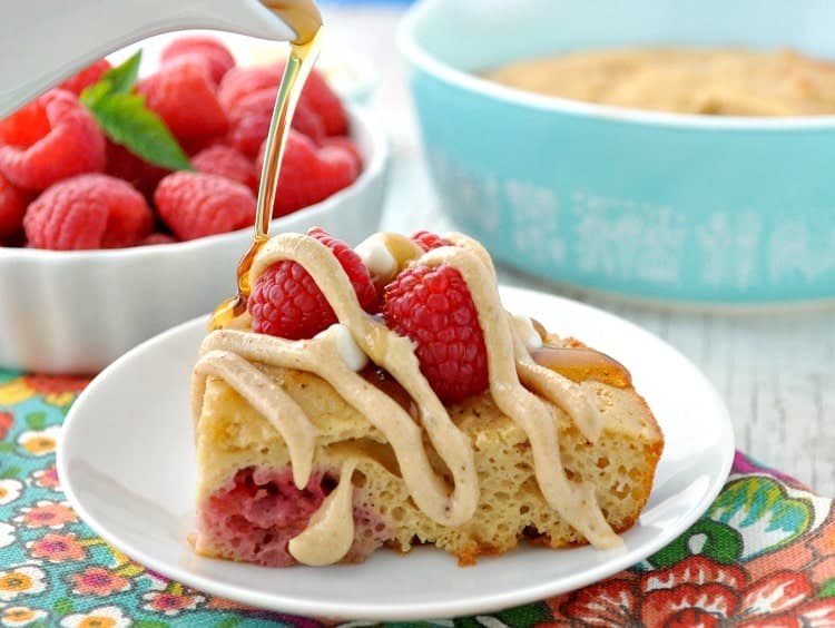 A close up of baked pancakes on a plate drizzled with syrup and topped with raspberries