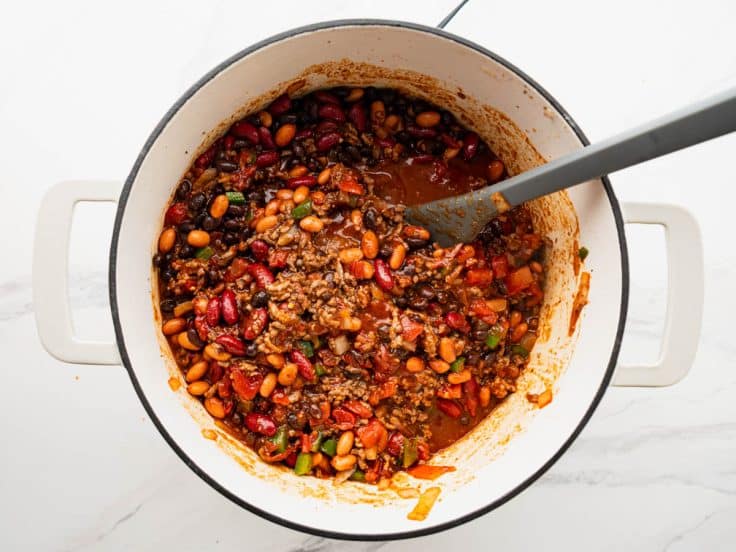 Stirring beans and remaining ingredients into a pot of cowboy chili.