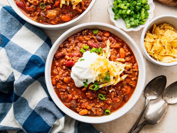 Horizontal overhead shot of a bowl of the best cowboy chili recipe with a side of toppings.