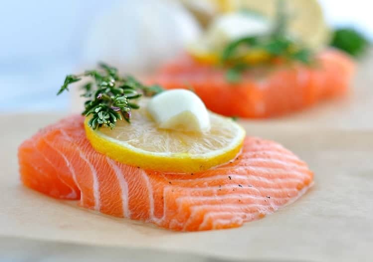 A close up of a salmon fillet on baking parchment with herbs, garlic and lemon