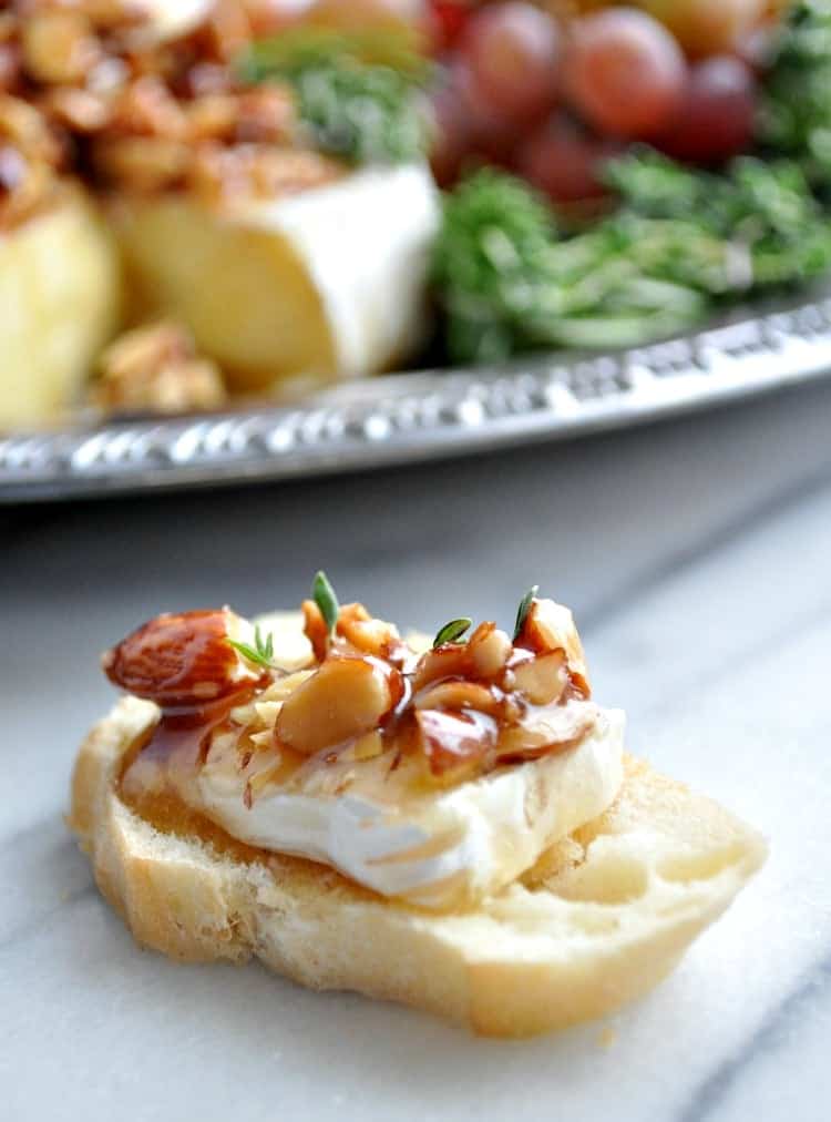 Close up image of baked brie with honey and almonds on a slice of baguette