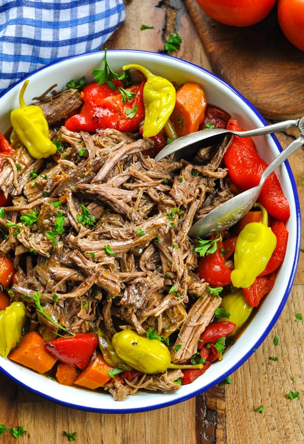 Overhead image of serving bowl with shredded Italian slow cooker roast beef and tongs