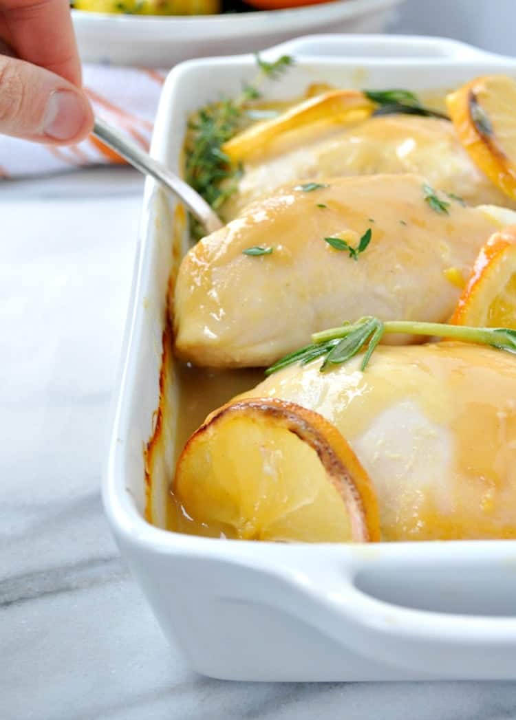 A close up of citrus and herb baked chicken in dish getting picked up with a serving spoon