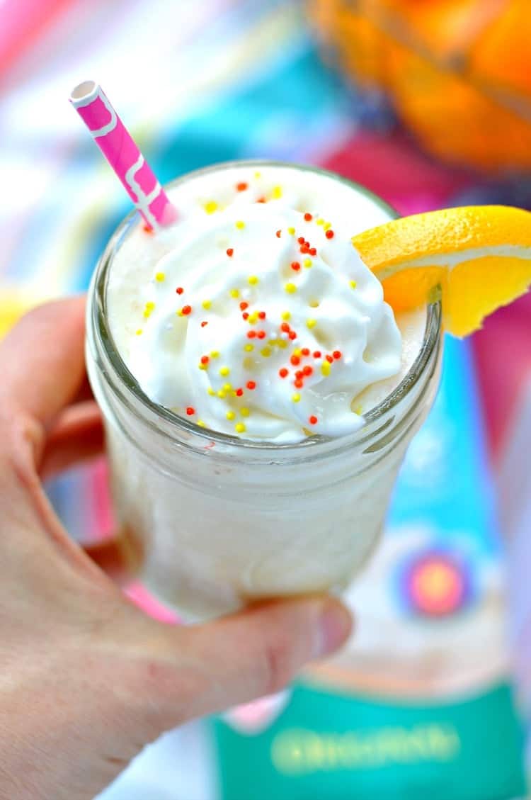 A close up of an orange smoothie in a jar with a straw and topped with cream