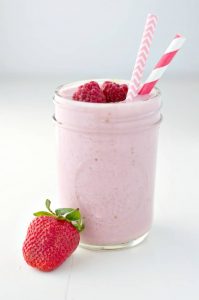 A side shot of a berry smoothie in a jar with 2 raspberries on top