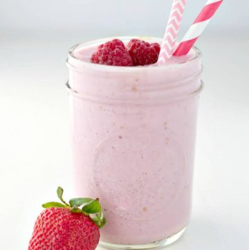 A side shot of a berry smoothie in a jar with 2 raspberries on top