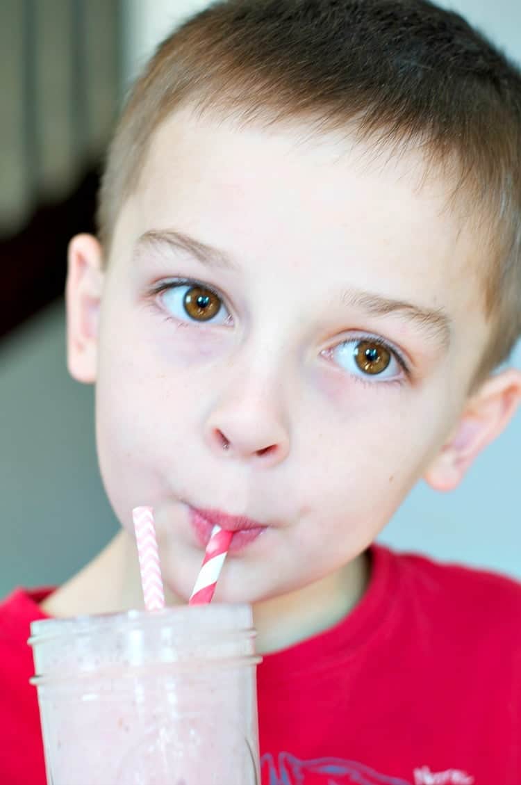 A small boy drinking a berry smoothie jar