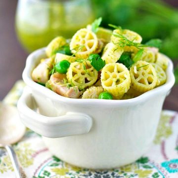 White bowl full of chicken pesto pasta with fresh herbs on top