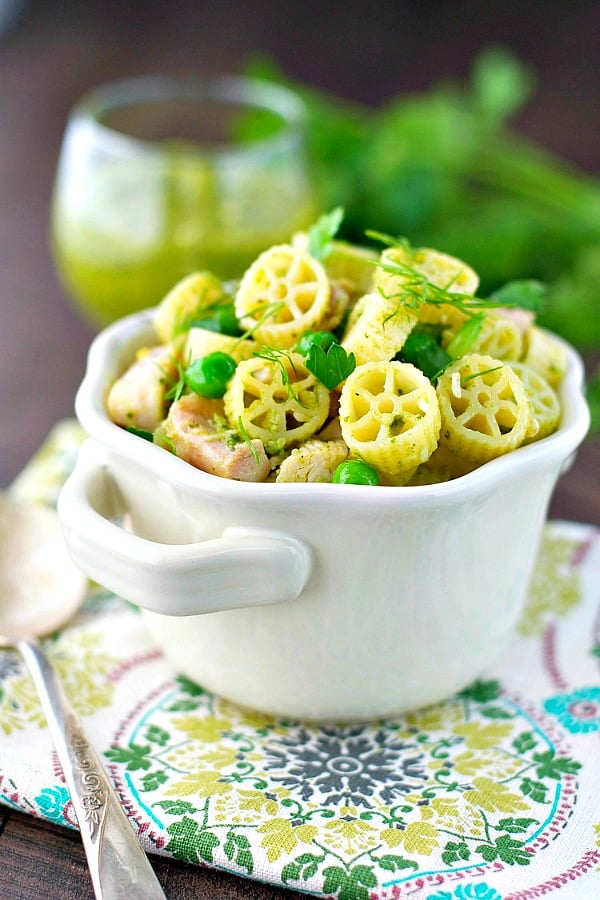 White bowl full of chicken pesto pasta with fresh herbs on top